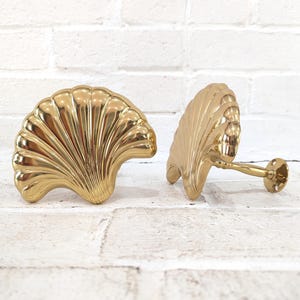 Può includere: Due fermatende dorati a forma di conchiglia. I fermatende sono in metallo e hanno una finitura lucida. Il design a conchiglia presenta creste e curve dettagliate, aggiungendo un tocco di eleganza costiera a qualsiasi stanza.