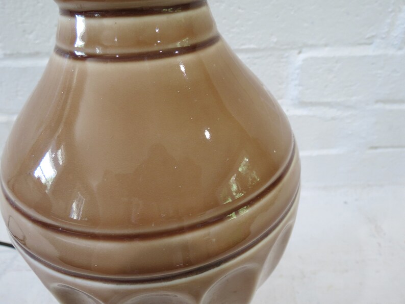 May include: A brown ceramic lamp base with a textured, ribbed design. The base has a glossy finish and a wide, rounded shape.
