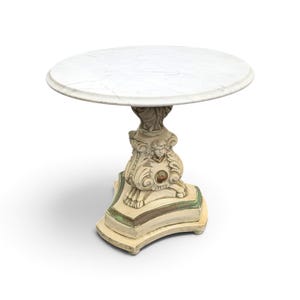 May include: A round side table with a white marble top featuring grey veining. The pedestal base is painted in an off-white finish with green accents and features a carved cherub face detail and ornate scrollwork on a tripod base.