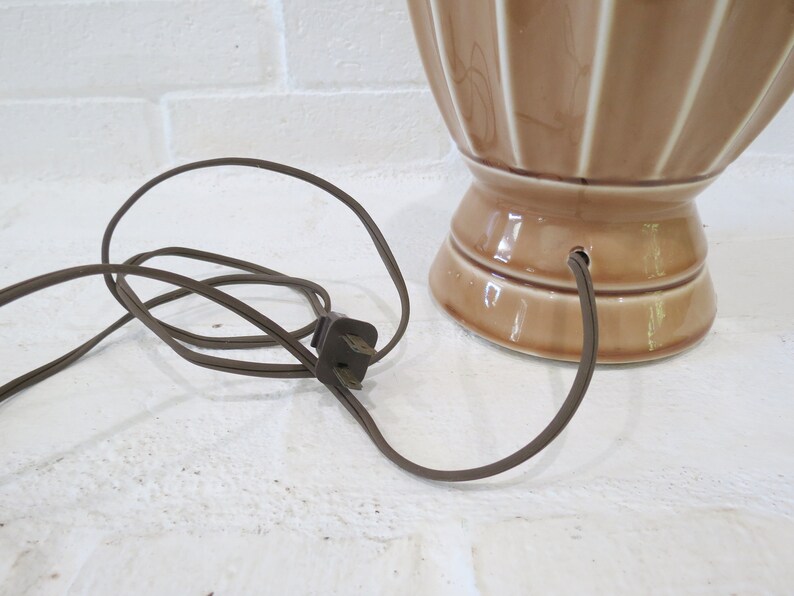 May include: A brown ceramic table lamp with a cord and plug. The lamp has a fluted design and a wide base.
