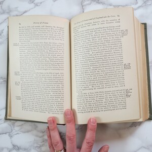 K&ouml;nnte beinhalten: Ein ge&ouml;ffnetes Buch mit gr&uuml;nem Einband. Die Seiten sind vergilbt und der Text ist schwarz. Das Buch tr&auml;gt den Titel "Geschichte Frankreichs" und "Die K&ouml;nige von Frankreich und England nehmen das Kreuz".