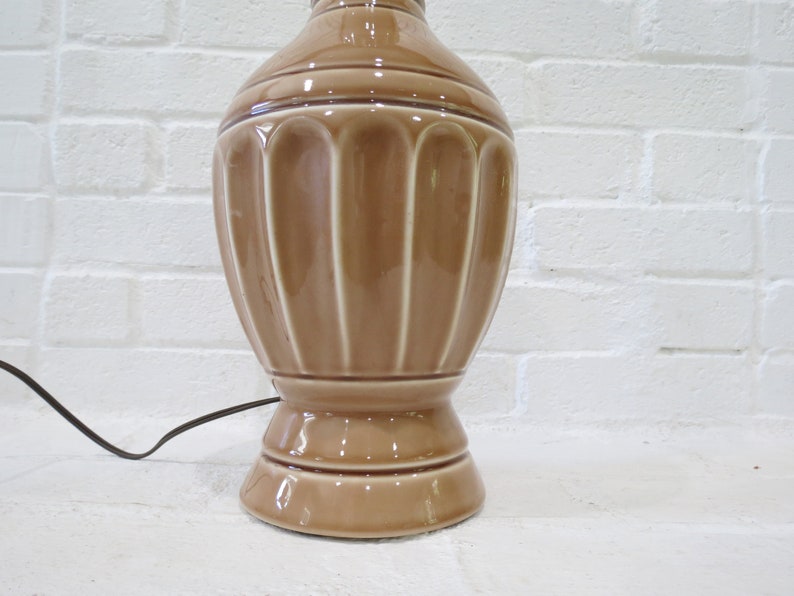 May include: A brown ceramic table lamp with a fluted design. The lamp has a round base and a cord.