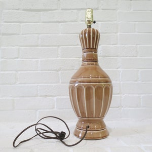 May include: A brown ceramic table lamp with a white ribbed design. The lamp has a gold-colored metal base and a brown cord.
