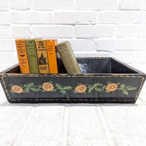 Puede incluir: Una bandeja rectangular de madera negra con un diseño floral y varios libros antiguos. Los libros tienen varios colores y títulos, incluyendo "A Man Goes Forth" y "The Call of the Canyon."