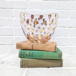 May include: A clear glass bowl with a wavy rim and gold polka dots. The bowl is sitting on top of a stack of three books.