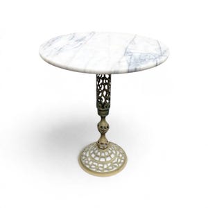 May include: A round side table featuring a white marble top with grey veining. The table is supported by a single, ornate metal pedestal base with an intricate, openwork filigree design in a muted, light metallic finish.