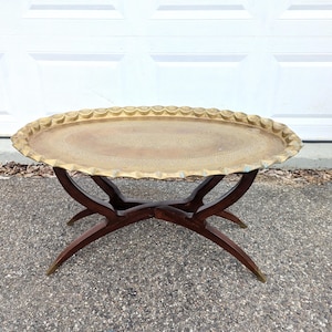 Puede incluir: Mesa auxiliar ovalada con bandeja de latón y borde festoneado. La bandeja se apoya sobre una base de madera oscura con patas curvas y punteras de latón. Una pieza vintage para el salón.