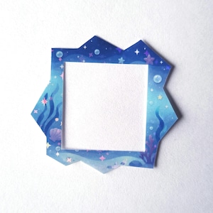 Op de afbeelding: Een vierkant frame met een onregelmatige, grillige buitenrand met een onderwaterthema. Het ontwerp toont blauwtinten met illustraties van zeewier, schelpen, bubbels en kleine roze en witte sterren tegen een diepblauwe achtergrond.
