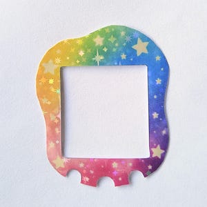 Op de afbeelding: Een regenboogkleurige, gestanste lijst met een vierkante opening. De lijst heeft een golvende bovenrand en drie gebogen uitsparingen aan de onderkant. De lijst is versierd met stervormige en diamantvormige holografische accenten.
