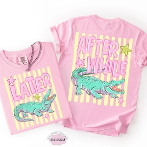 May include: Two pink t-shirts with the words "LATER" and "AFTER WHILE" in pink bubble letters. Each shirt features a teal alligator graphic with an open mouth, set against yellow stripes and stars. The shirts are Comfort Colors brand.