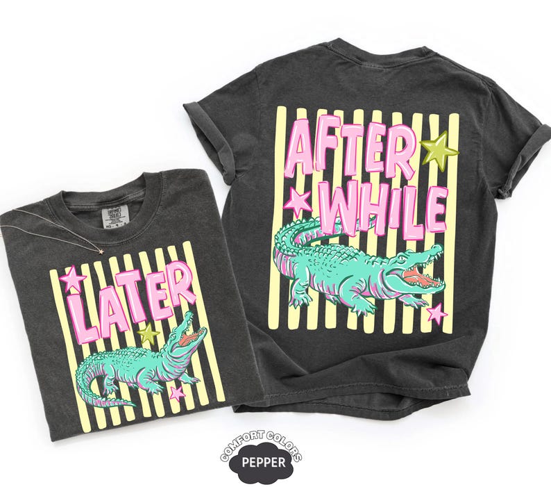 May include: Two dark gray t-shirts with a graphic of a turquoise alligator and the text "LATER" and "AFTER WHILE" in pink letters. The shirts have yellow vertical stripes and star accents.