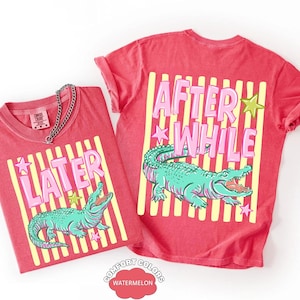 May include: Two red t-shirts with a graphic design featuring a teal alligator, pink text, and yellow stripes. One shirt says "LATER" and the other says "AFTER WHILE". The shirts are labeled "Comfort Colors Watermelon".