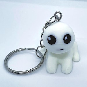 May include: A white, small, four-legged creature figurine keychain with a round head, large black circular eyes, and a thin horizontal line for a mouth. The figure is attached to a silver-colored metal split ring by a short metal chain.