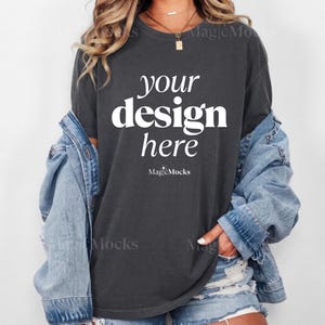 May include: A charcoal gray crewneck t-shirt featuring the white text "your design here" printed on the front, layered under a light blue denim jacket with distressed denim shorts, showcasing a casual and versatile apparel combination.