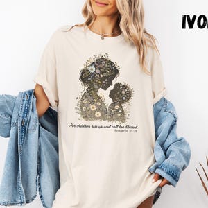 May include: Ivory-coloured t-shirt with a floral silhouette of a mother and child. The design includes the text "Her children rise up and call her blessed. Proverbs 31:28". The word "IVORY" is printed in bold, black letters.