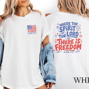 Könnte beinhalten: Ein weißes T-Shirt mit einer kleinen amerikanischen Flaggengrafik und dem Text 2 COR. 3:17 auf der linken Brust. Die Rückseite zeigt den Text WHERE THE SPIRIT OF THE LORD IS THERE IS FREEDOM mit einem Kreuz, Sternen und Blumen in Rot und Blau.