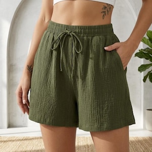 Puede incluir: Pantalones cortos verde oliva con cintura con cordón y bolsillos. Los pantalones cortos tienen una tela texturizada y arrugada. Ropa casual.