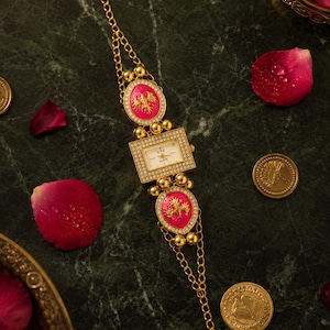 May include: Gold-coloured watch with a rectangular face and two pink, oval-shaped accents. The watch features a chain-link band and is adorned with small, round gold beads and clear crystals. The watch face displays the text "CTZ Quartz".