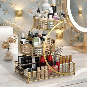 May include: A three-tiered gold metal wire storage organizer with a spiral frame design. The unit features a rectangular base tray and two circular upper baskets, filled with various skincare bottles, makeup brushes, and cosmetic containers.