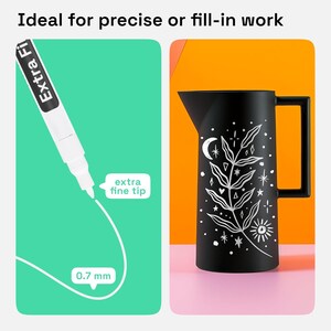 May include: A white paint marker with an extra fine 0.7 mm tip and a black matte pitcher featuring a white botanical illustration of a leafy branch, a crescent moon, and a sun. The text on the marker reads Extra Fine and the label reads extra fine tip.