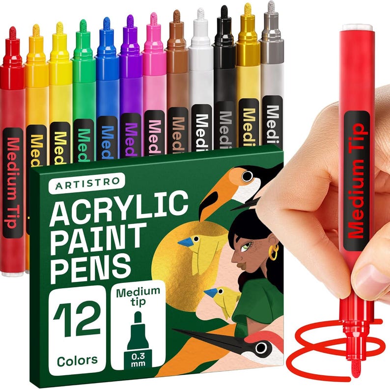 May include: A set of 12 acrylic paint pens in various colors, with a medium tip. The box features the brand name "ARTISTRO" and the text "ACRYLIC PAINT PENS". A hand holds a red pen, demonstrating its use.