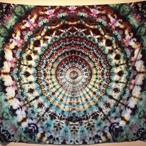 May include: A large square tapestry featuring a complex tie-dye mandala pattern. The design radiates from a central point in concentric circles of vibrant colors including deep teal, forest green, bright yellow, fiery orange, and dark brown.