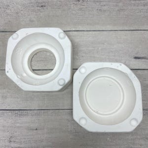 May include: Two white ceramic plaster molds for casting, featuring an octagonal exterior shape with rounded corners. One mold has a large circular center opening, while the other is a solid bowl-shaped cavity. Both pieces have small snowflake icons.