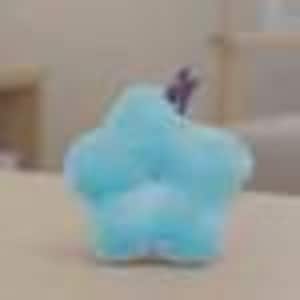 May include: A light blue, star-shaped plush toy with a small purple stem. The soft, fluffy toy is sitting on a light-colored surface. The toy is a whimsical decorative item.