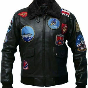 May include: Black leather jacket with multiple embroidered patches, including "Texas Dallas" and "Tomcat." The jacket features a black faux fur collar, two front pockets, and a ribbed hem and cuffs. A classic bomber jacket style.