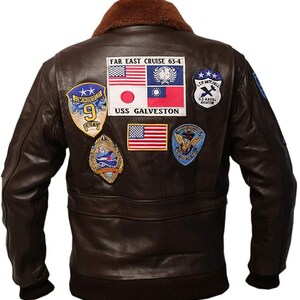May include: A brown leather bomber jacket with a brown fur collar. The back of the jacket features several embroidered patches, including flags and text that reads "FAR EAST CRUISE 63-4" and "USS GALVESTON". The jacket has a ribbed hem and cuffs.