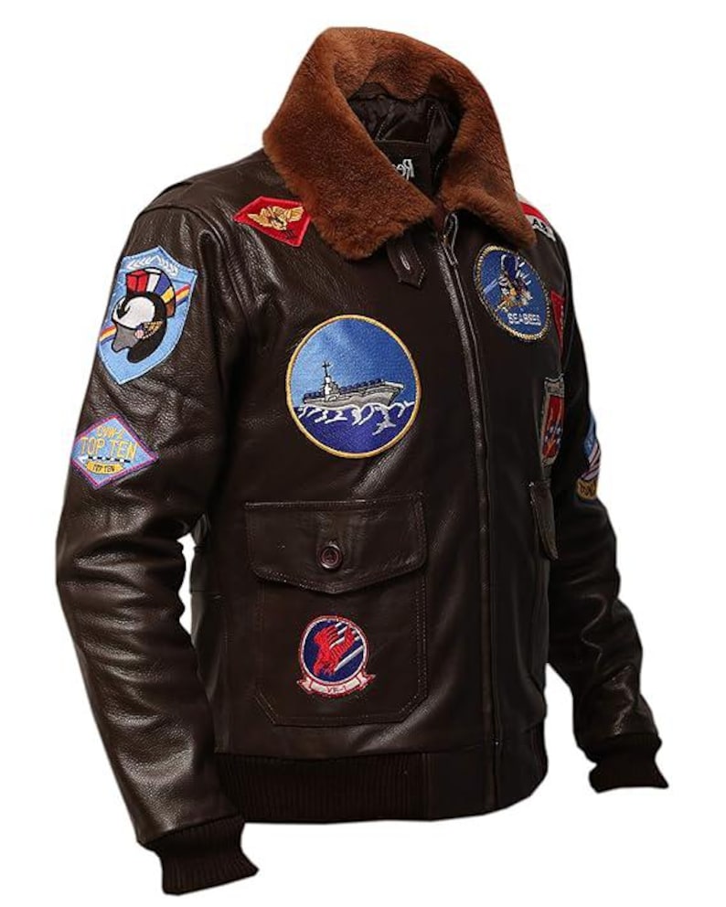 May include: Brown leather bomber jacket with a brown faux fur collar. The jacket features multiple embroidered patches, including a ship, eagle, and other military-themed designs. It has a ribbed hem and cuffs, and two front pockets.