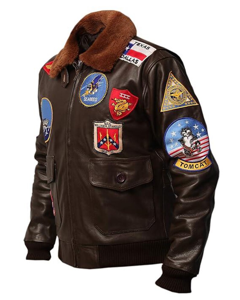 May include: A brown leather bomber jacket with a brown fur collar. The jacket features multiple embroidered patches, including "Texas Dallas", "Seabees", and "Tomcat". It has two front pockets and a ribbed cuff and hem.