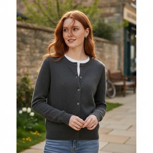 Peut inclure: Un cardigan gris anthracite avec un col rond et une fermeture boutonnée. Le pull à manches longues est porté sur un t-shirt blanc. Le cardigan a un motif texturé et est associé à un jean bleu.