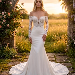 Könnte beinhalten: Ein weißes Brautkleid mit Meerjungfrau-Silhouette. Das schulterfreie Oberteil hat Spitzendetails und lange Ärmel. Das Kleid hat eine lange Schleppe und wird in einem Garten mit einem Torbogen und Blumen getragen.