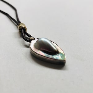 Peut inclure: Un collier avec un pendentif en forme de larme, composé d'une perle sertie dans une coquille d'ormeau et d'argent. Le collier est fait d'un cordon en cuir noir et d'accents dorés.