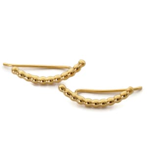 May include: A pair of gold ear cuffs with a beaded design. The cuffs are curved and have a simple, minimalist style.