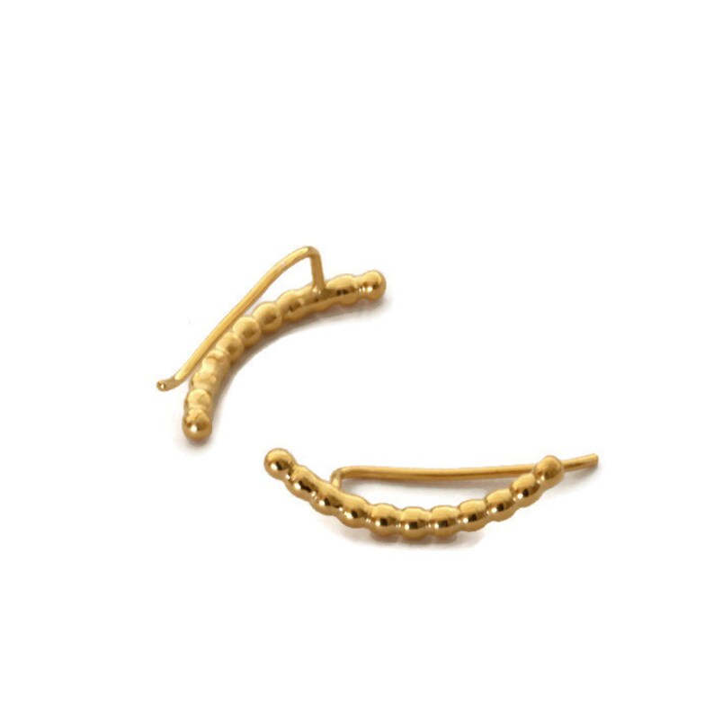 May include: A pair of gold ear cuffs with a beaded design. The cuffs are curved and have a simple, minimalist style.