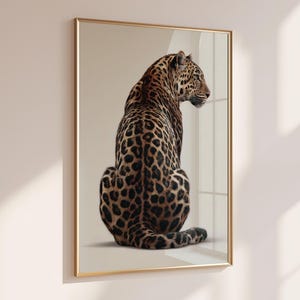 Può includere: Una stampa artistica da parete incorniciata che raffigura un leopardo realistico seduto e rivolto verso destra. Il leopardo ha un mantello marrone dorato con distinte rosette e macchie nere. L'opera è racchiusa in una sottile cornice color oro.