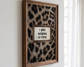 Peut inclure: Une décoration murale rectangulaire présentant un fond à motif léopard marron et noir, encadrée par un cadre en bois foncé. Au centre se trouve une plaque rectangulaire blanche plus petite avec le texte noir "I HAVE NOTHING TO WEAR".