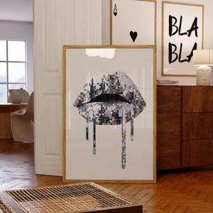 May include: A framed vertical wall art print featuring a graphic illustration of lips covered in silver mirrored disco ball tiles. The lips are depicted with a dripping effect, with several vertical strands of mirrored tiles hanging down.