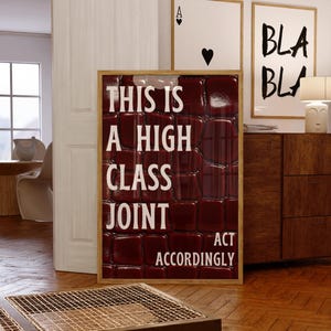 May include: A rectangular framed wall art piece featuring a deep red, glossy, crocodile-embossed texture background. The white text reads: THIS IS A HIGH CLASS JOINT ACT ACCORDINGLY. The frame is a light-toned wood, and the print has a reflective finish.