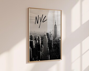 Peut inclure: Une impression murale verticale encadrée présentant une photographie en noir et blanc de la ligne d'horizon de New York, incluant l'Empire State Building. Les lettres NYC sont écrites en gras, en noir, dans un style manuscrit.