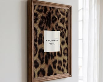 Peut inclure: Une œuvre d'art murale rectangulaire dans un cadre en bois brun foncé avec un fond à motif léopard. Au centre se trouve un carré blanc portant le texte noir IF YOU WANT IT, GET IT. L'œuvre est exposée sur un mur blanc.