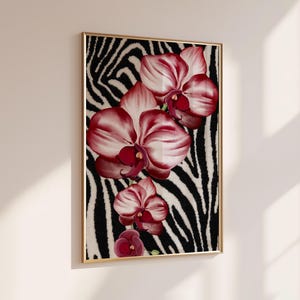 Peut inclure: Une impression d'art murale rectangulaire dans un cadre doré fin présentant un arrangement vertical de fleurs d'orchidées magenta foncé et blanches sur un fond à motif de rayures zébrées noir et blanc contrasté, fixée sur un mur neutre.