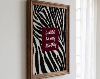 Peut inclure: Une œuvre d'art murale rectangulaire dans un cadre en bois brun foncé avec un motif de rayures zébrées noir et blanc. Au centre se trouve un carré bordeaux uni avec le texte blanc en cursive, Grateful for every little thing.