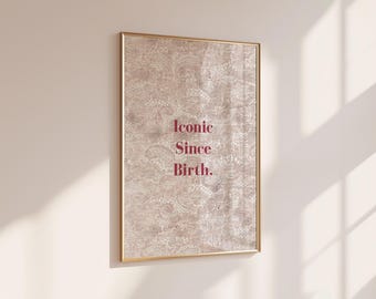 Peut inclure: Une affiche murale rectangulaire dans un cadre doré fin, présentant un fond beige avec un motif cachemire en dentelle blanche. Le texte "Iconic Since Birth." est imprimé au centre en police serif rouge foncé.