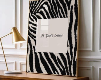Peut inclure: Une œuvre d'art murale rectangulaire encadrée présentant un motif de rayures zébrées noires et blanches entourant un carré blanc central. Le texte In God's Hands est imprimé en écriture noire au centre du carré blanc. Le cadre est fin et doré.