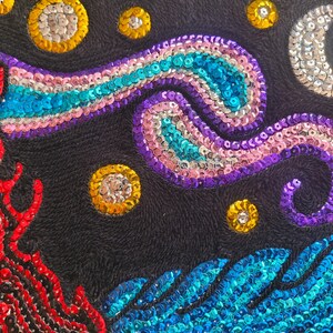 Könnte beinhalten: Eine schwarze Stoffoberfläche mit aufwendiger Paillettenstickerei. Das Design zeigt eine rote flammenartige Form, einen wirbelnden violett-blauen Nebel, einen silbernen Halbmond und mehrere goldene Paillettensterne auf dem dunklen Hintergrund.