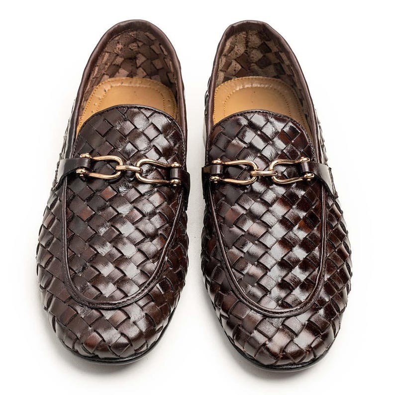 May include: A pair of dark brown woven leather loafers featuring a glossy finish and a gold-toned metal horsebit detail across the vamp. The shoes have a rounded toe design and a tan interior lining, showcasing a structured and slip-on style.