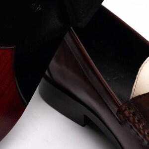 Pu&ograve; includere: Primo piano di un paio di mocassini in pelle marrone. Le scarpe hanno un design classico con una finitura lucida. Le suole sono nere e l'interno &egrave; di colore chiaro. La taglia 42 &egrave; visibile sulla suola.